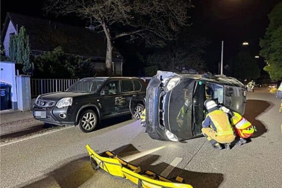Ein umgekippter Honda Jazz nach Unfall, Fahrer eingeklemmt, Einsatzkräfte im Hintergrund.