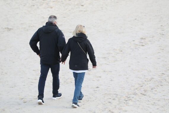 Paar spaziert am Strand, Symbol für Unterstützung und Zusammenhalt in schwierigen Zeiten.