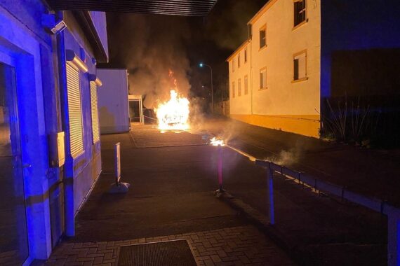 Ein brennender Pkw verursacht hohen Schaden, Feuerwehr im Einsatz, Gebäude ebenfalls betroffen.
