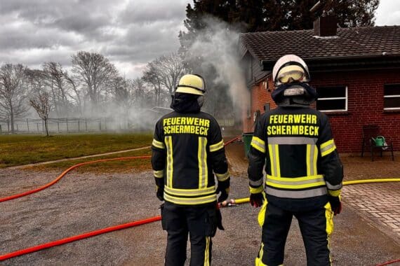 Feuerwehrleute bekämpfen einen Zimmerbrand in einem Anbau, starke Rauchentwicklung sichtbar.