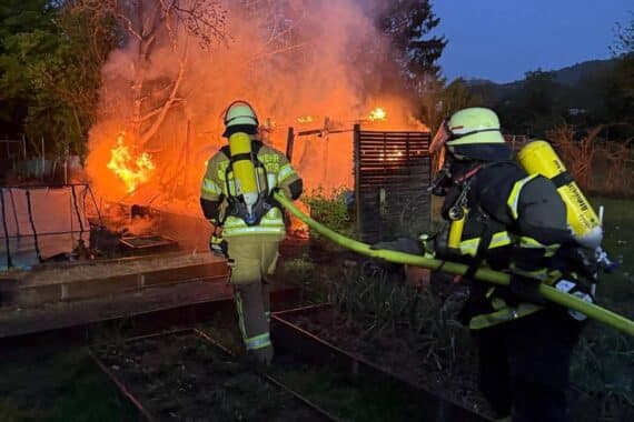 Feuerwehrleute löschen Brand in Gartenhütte, Rauch steigt auf, Einsatzkräfte im Einsatz.