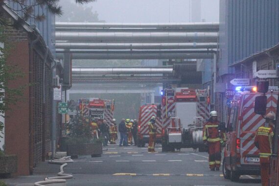 Feuerwehrleute bekämpfen Brand in Industriebetrieb, Rauch und Flammen sichtbar, Einsatzkräfte im Alarmmodus.