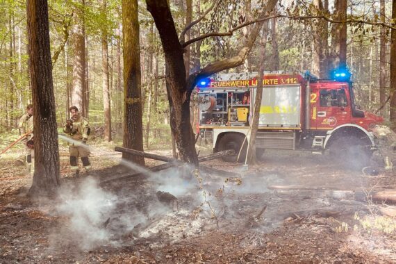 Brennendes Holz-Tipi im Wald, Feuerwehr-Löscharbeiten, erhöhter Brandgefahr, Einsatzkräfte am Werk.