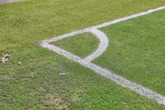 Ecke eines Fußballfeldes, umgeben von Spannung und Konflikt, während Spieler und Zuschauer kämpfen.