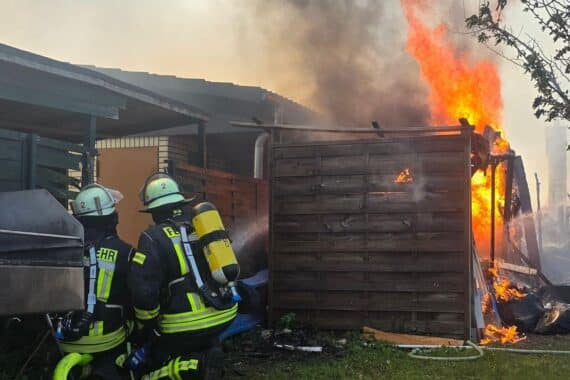 Feuerwehr bekämpft Brand in Laubenkolonie, mehrere Lauben stehen in Flammen, eindrucksvolles Löschgeschehen.