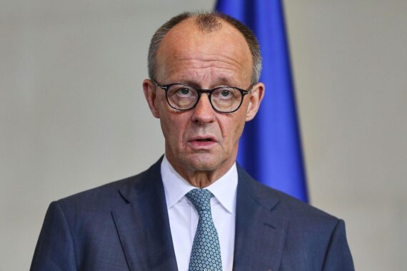 Friedrich Merz am Rednerpult, symbolisiert diplomatische Bemühungen für Frieden im Iran.