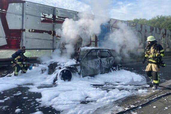 Auto brennt auf Autobahn, Feuerwehr löscht Brand, Rauchentwicklung sichtbar, Rettungsgasse gebildet.
