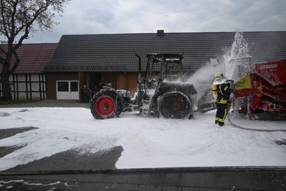 Brand eines Traktors auf der Straße, Feuerwehr im Einsatz, rauchende Flammen, Polizei vor Ort.