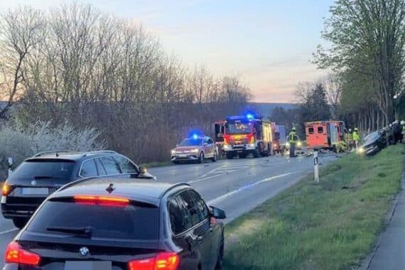 Unfallstelle mit Trümmern, beschädigten Fahrzeugen und Einsatzkräften der Feuerwehr. Verletzte Personen vorhanden.