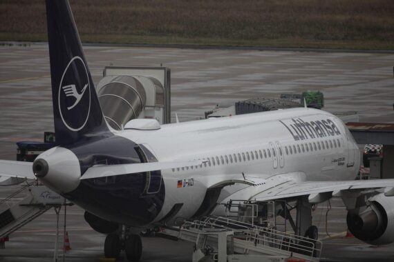 Lufthansa-Maschine vor streikender Kulisse, die Auswirkungen des Streiks auf Reisende reflektierend.