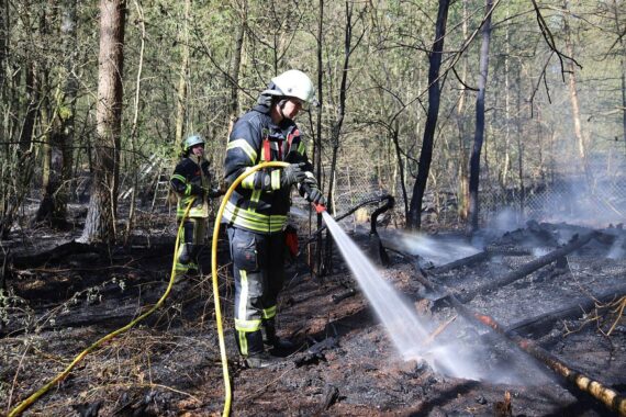 Waldbrand mit Flammen und Rauch, Feuerwehr im Einsatz, evakuierte Besucher im Vordergrund.