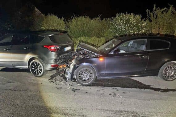 Unfallstelle mit beschädigten Fahrzeugen, Polizei und umherstehende Zeugen nach nächtlichem Vorfall.