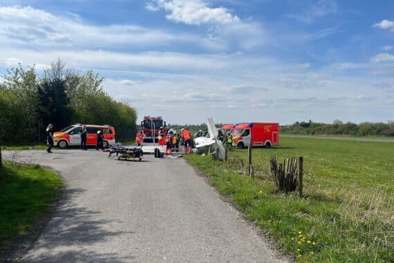 Motorsiertes Kleinflugzeug auf Wiese, Rettungskräfte im Einsatz, Unfallstelle abgesperrt.