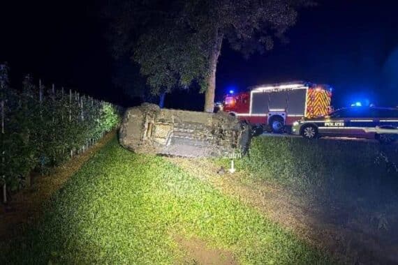 Unfallstelle mit einem umgekippten Auto, Verkehrsschild und Feuerwehrmaßnahmen.