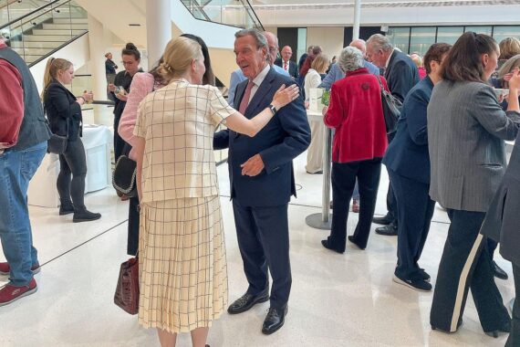 Gerhard Schröder vom Rücken, symbolisch vor einem Hintergrund von Frieden und Konflikt.
