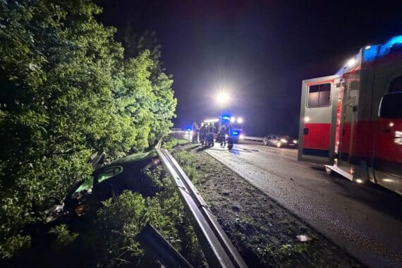 Unfallauto hinter Leitplanke, Feuerwehr und Ersthelfer im Einsatz, nachts auf Autobahn A57.