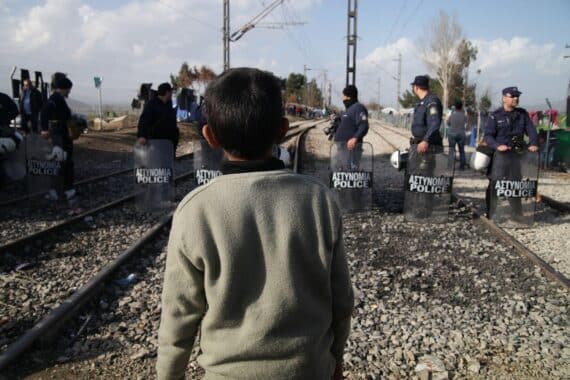Ein Flüchtlingsjunge steht traurig an einer EU-Außengrenze, symbolisiert Hoffnung und Entbehrung.