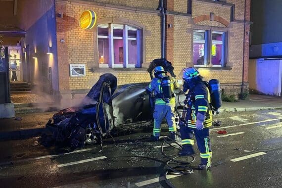 Feuerwehrleute mit Atemschutz löschen brennendes Auto vor einem Gebäude in Weinheim.