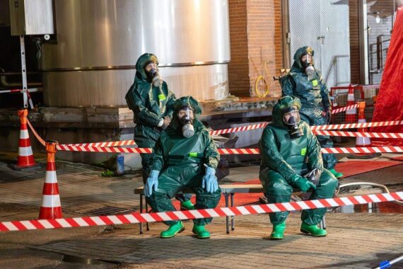 Einsatzkräfte der Feuerwehr bei Gefahrgutaustritt auf einem Betriebsgelände, Chemikalienschutzanzüge sichtbar.