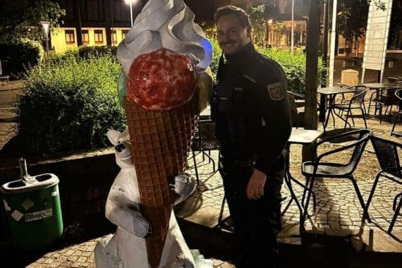 Überdimensionale Eiswaffel steht stolz vor Eisdiele, umgeben von neugierigen Passanten.