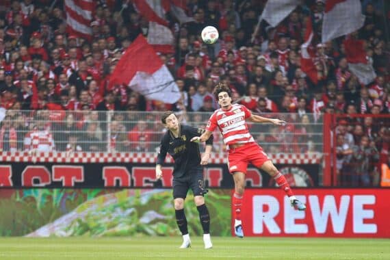 Bundesliga-Spieler jubeln nach Union Berlins 4:0-Sieg gegen Augsburg, finale Tabellenplatzierungen im Hintergrund.