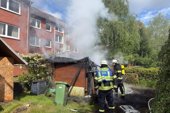 Holzschuppen brennt lichterloh; Feuerwehr kämpft gegen Flammen, schützt angrenzende Gebäude und Gärten.