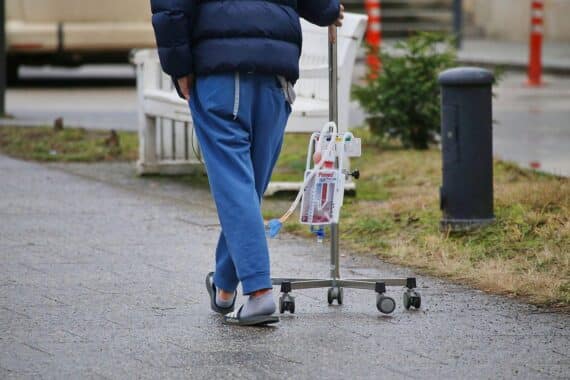 Patient mit Infusionsständer, symbolisiert die finanziellen Herausforderungen in der Pflegeversicherung.