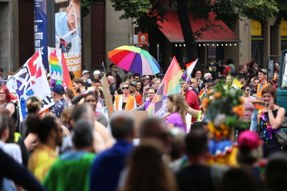 Bunte Parade mit LGBTIQ+-Flaggen, Menschen feiern Vielfalt und fordern Gleichberechtigung.