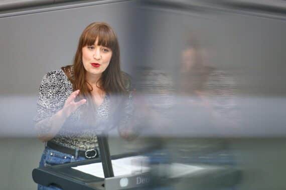 Heidi Reichinnek diskutiert Diätenkürzungen für Bundestagsabgeordnete, Umrisse von Parlamentariern im Hintergrund.