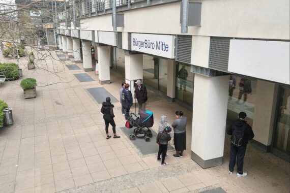 Menschen vor einem Bürgerbüro, wartend auf Einbürgerung, symbolisiert den Rekord an Einbürgerungen.