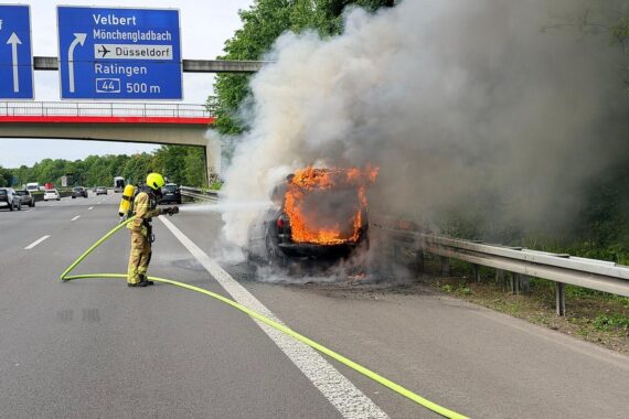 Flammendes Auto auf Autobahn, Feuerwehr im Einsatz, Polizei reguliert den Verkehr.