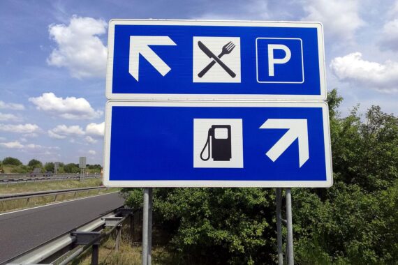 Tankstelle mit Preistafel und Menschen, die sprit kaufen oder auf den Preis achten.