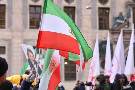 Protestierende Menschen mit Schildern gegen den Iran, vor einer politischen Kulisse in Berlin.
