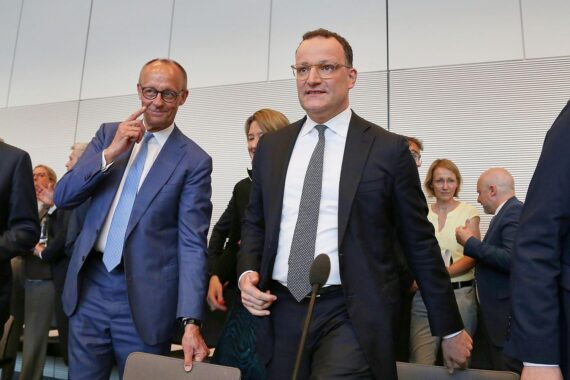 Friedrich Merz und Jens Spahn lächeln zusammen bei einer politischen Veranstaltung in Berlin.