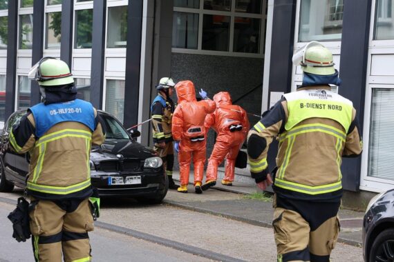 Feuerwehr im Einsatz mit Schutzanzügen nach möglichem chemischen Vorfall in Bürogebäude.