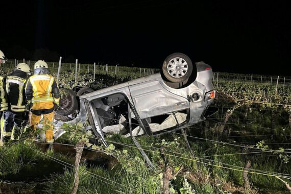 Unfallauto im Weinberg, welche nach Überschlag auf dem Dach liegt, mit Polizeiauto daneben.
