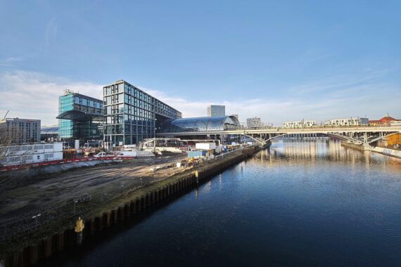 Berliner Hauptbahnhof mit Sonnenstrahlen, blauen Himmel und Wolken, symbolisiert trockenes, warmes Wetter.