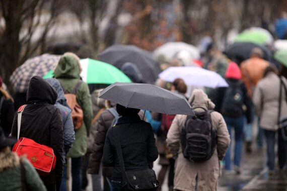 Menschen mit Regenschirmen gehen durch eine trübe, regnerische Landschaft in Mecklenburg-Vorpommern.
