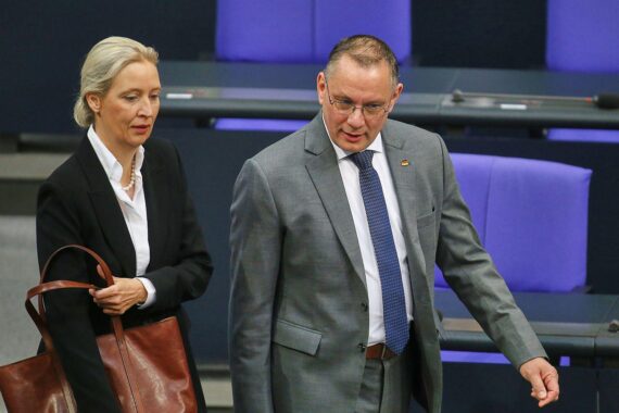 AfD-Politiker auf Podium, Umfrageergebnisse im Hintergrund, politische Stimmung in Deutschland.