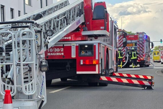 Feuerwehr löscht Zimmerbrand, Einsatzkräfte retten Person, Rauch dringt aus Mehrparteienhaus.