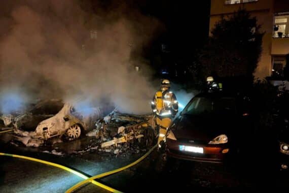 Zwei verbrannte Autos bei Nacht, Feuerwehr im Einsatz zum Löschen des Brandes.