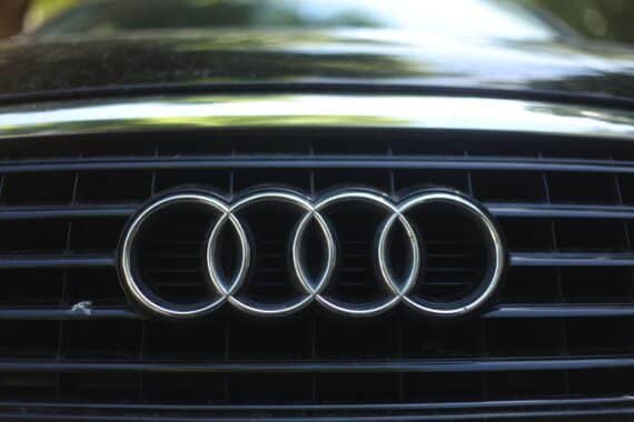 Audi-Logo neben Fahrzeugproduktion, symbolisiert Reduzierung der Verkaufsziele und Marktunsicherheit.