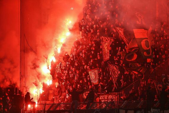 Fans feuern mit Pyrotechnik in einem Stadion, eine Herausforderung für Sicherheitskonzepte.