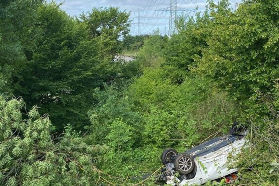 Wrack eines Autos, beschädigte Baumkrone, Unfallstelle auf Autobahn mit Polizeieinsatz.