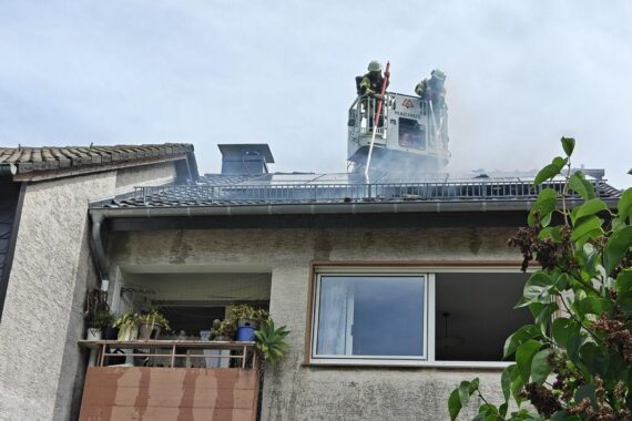 Feuerwehr löscht Brand im Dachbereich eines Wohnhauses, starke Rauchentwicklung sichtbar.