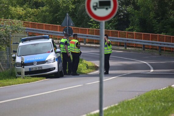 Verkehrskontrolle an einer Grenze, Beamte überprüfen Fahrzeuge, symbolisiert Sicherheit und politische Entscheidungen.
