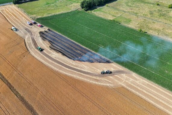 Flammen auf einem Feld, Feuerwehr im Einsatz, Drohne überwacht die Brandbekämpfung.