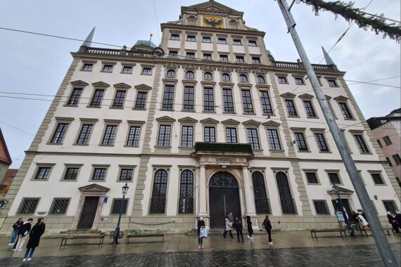 Rathaus Augsburg mit protestierenden Bürgern für bessere Fernverkehrsanbindung und Mobilität.