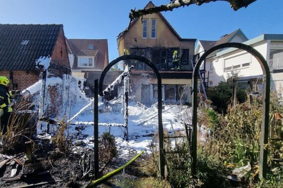 Feuerwehrlöscharbeiten am stark beschädigten Wohnhaus mit rauchenden Trümmern und abgerissenen Fenstern.