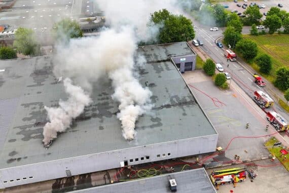 Rauchentwicklung und Feuerwehrleute bei Brandbekämpfung in einer Lagerhalle im Industriegebiet.